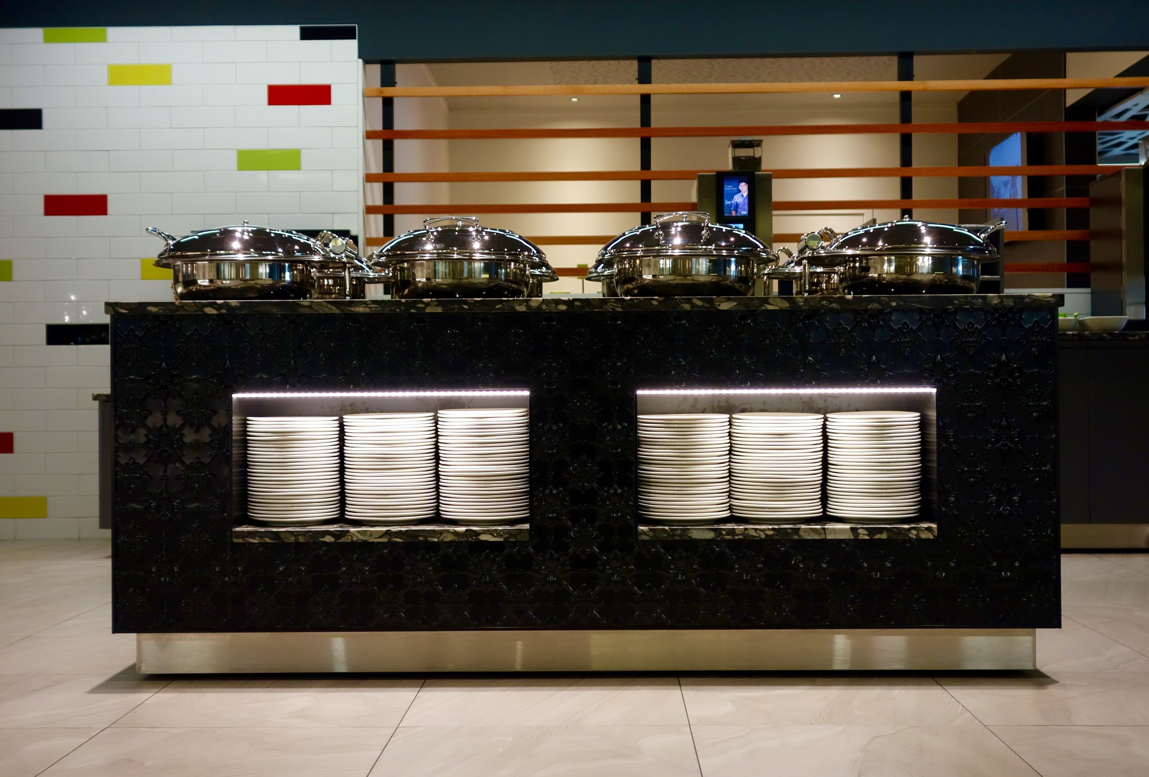 A buffet setup with multiple serving stations, each with a covered serving dish and stacked plates.