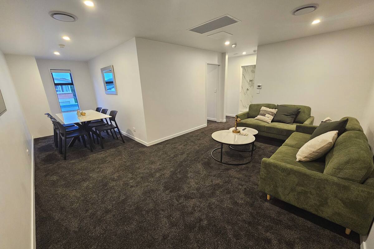 Una sala de estar moderna con un sofá verde, una mesa de centro redonda y un comedor con mesa y sillas.
