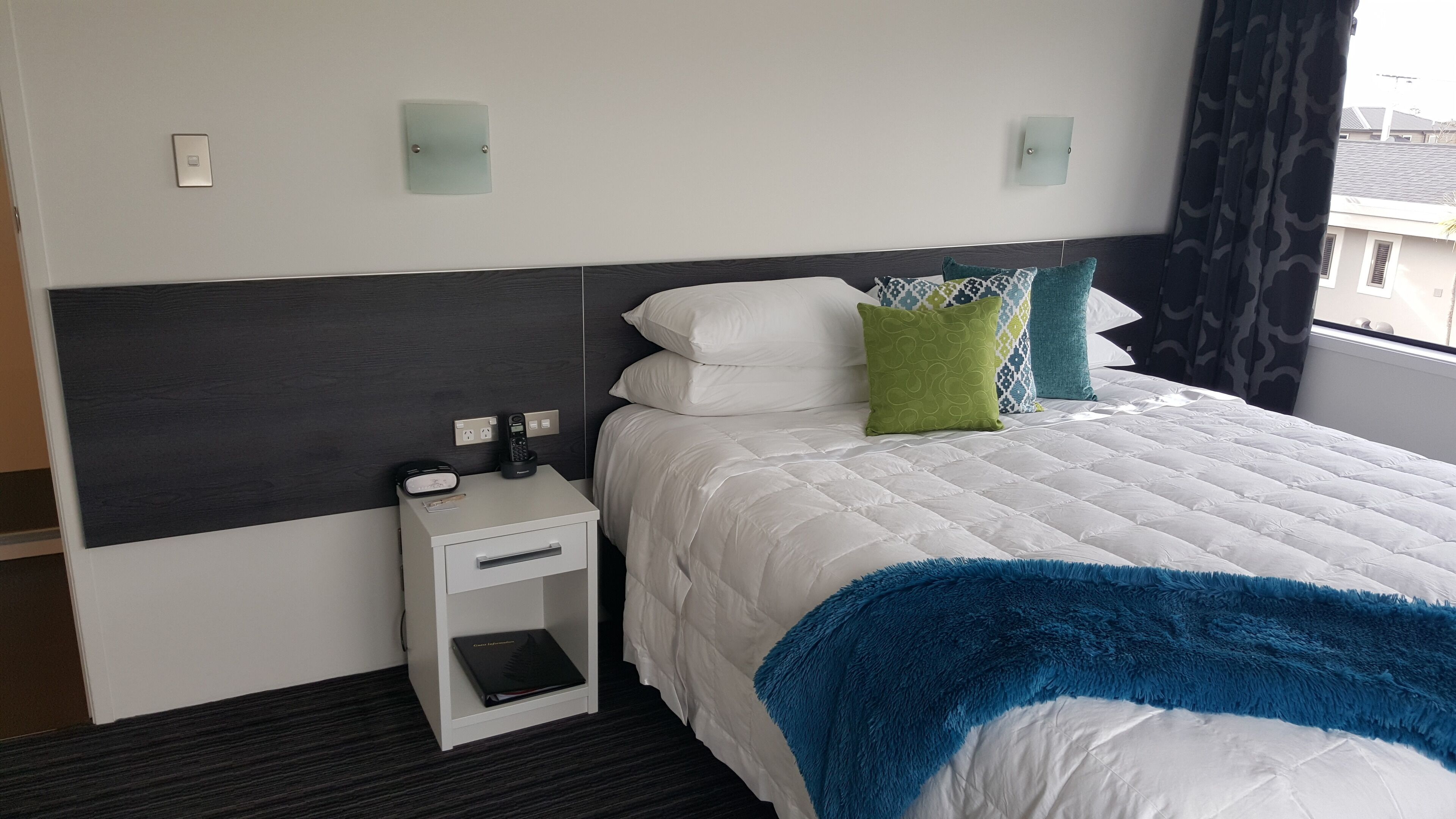 A hotel room with a bed, bedside table, and a window with curtains.