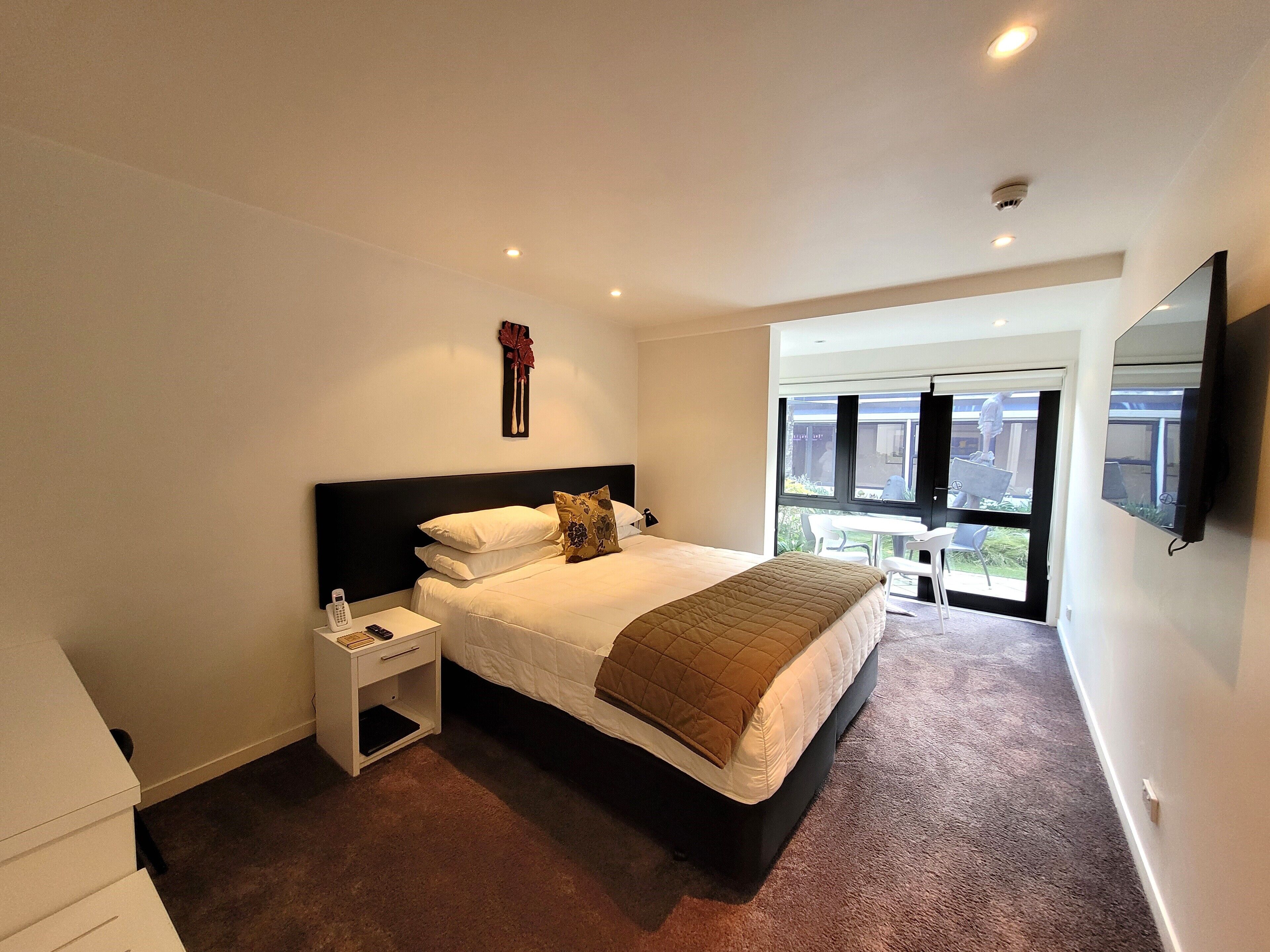 A modern bedroom with a large bed, bedside tables, a flat-screen TV, and a window with a view of the outside.