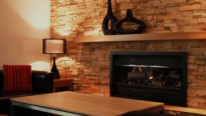 Una sala de estar con una pared de piedra, chimenea, sofá, mesa y lámpara.