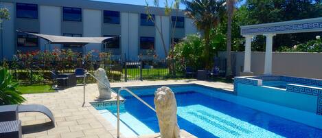 A swimming pool with a decorative lion statue, outdoor seating, and a building in the background.