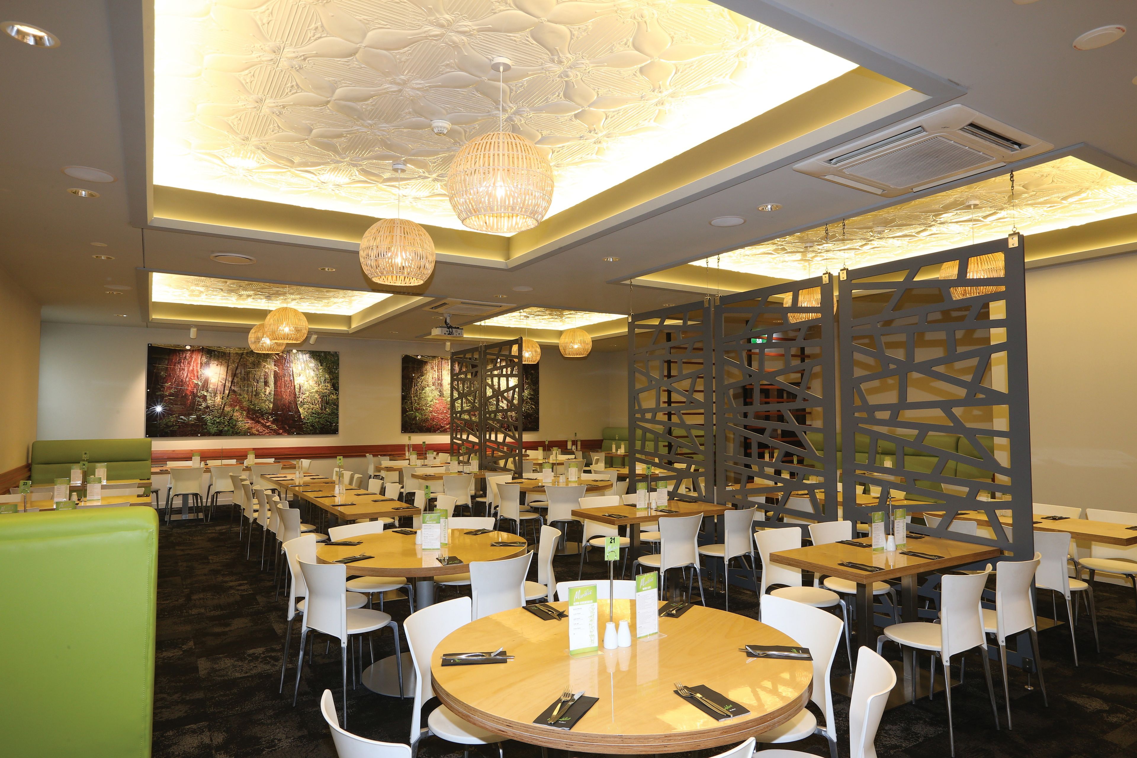A spacious dining area with round tables and white chairs, featuring ceiling lights and a decorative wall.