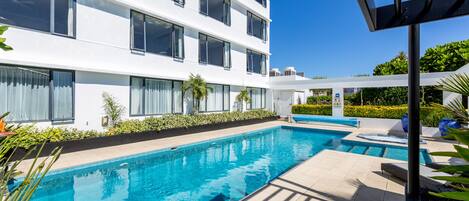 A modern hotel with a swimming pool, outdoor seating, and a well-maintained garden.