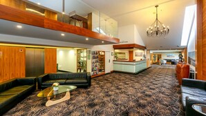 Un vestíbulo de hotel con alfombra estampada, sofás de cuero negro, una mesa de centro de vidrio y un mostrador de recepción.