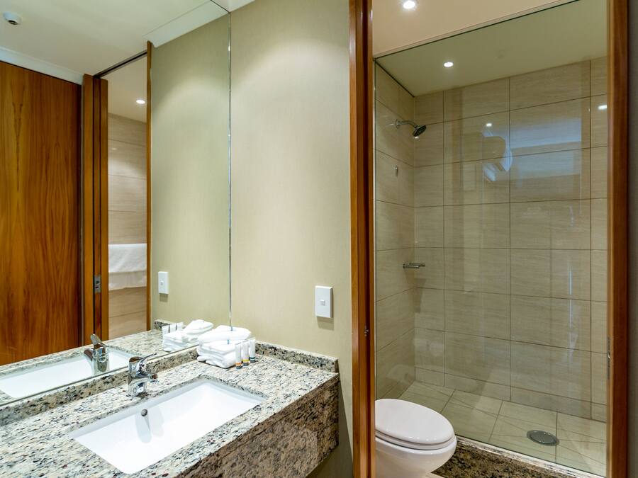 A hotel bathroom with a granite countertop sink, a mirror, a toilet, and a glass-enclosed shower.