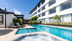 Un hotel moderno con piscina, tumbonas y bañera de hidromasaje.