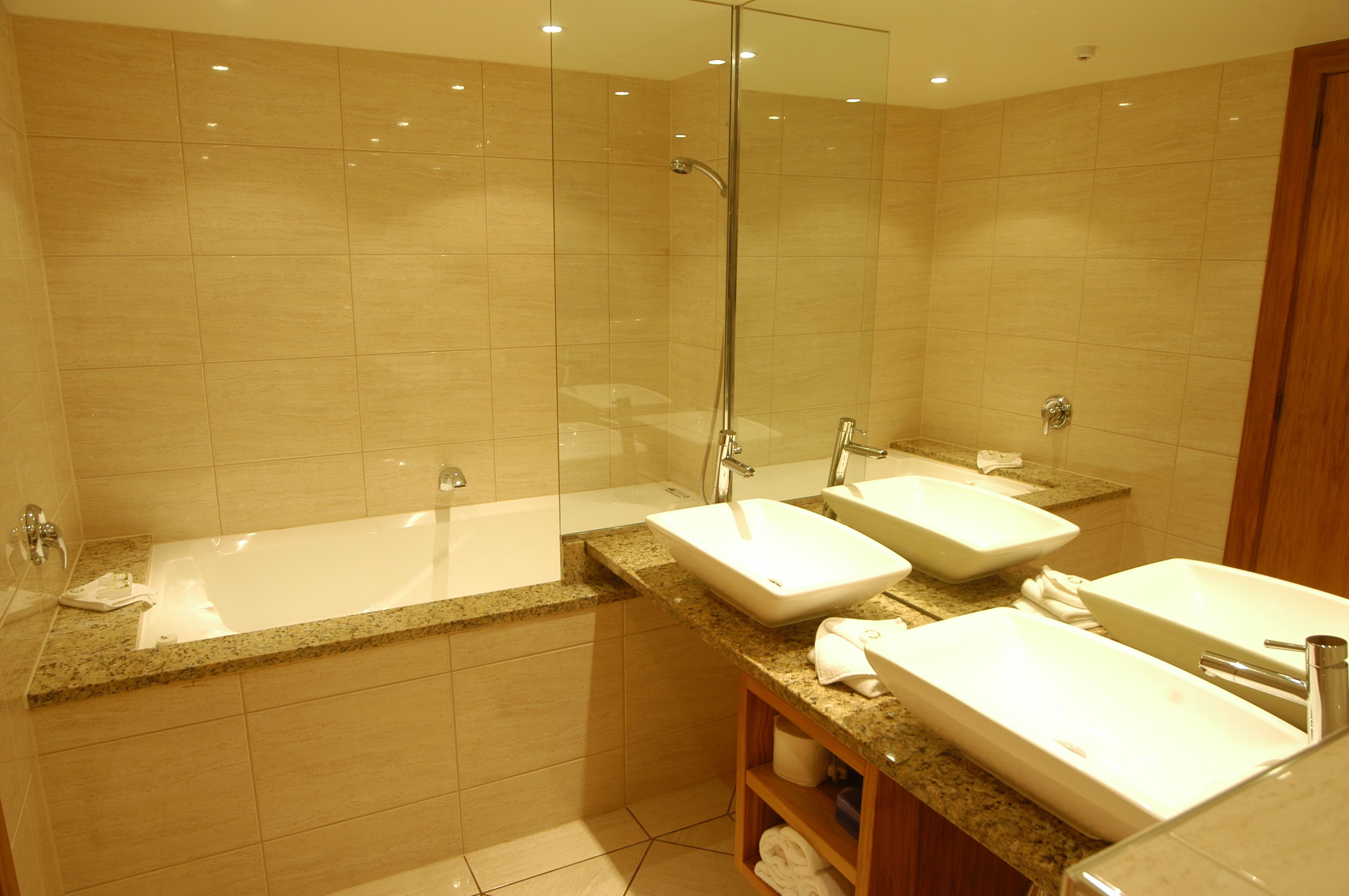 Un baño moderno con ducha de vidrio, una bañera independiente y dos lavamanos con encimeras de granito.