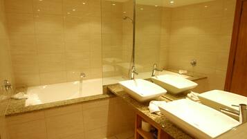 Un baño moderno con ducha de vidrio, una bañera independiente y dos lavamanos con encimeras de granito.