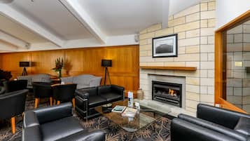 A modern lobby with leather seating, a glass coffee table, a fireplace, and a wooden accent wall.
