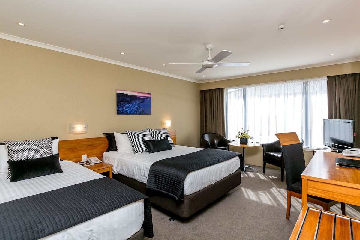 Ein Hotelzimmer mit zwei Betten, einem Schreibtisch, einem Sessel, einem Fernseher und einem Deckenventilator.