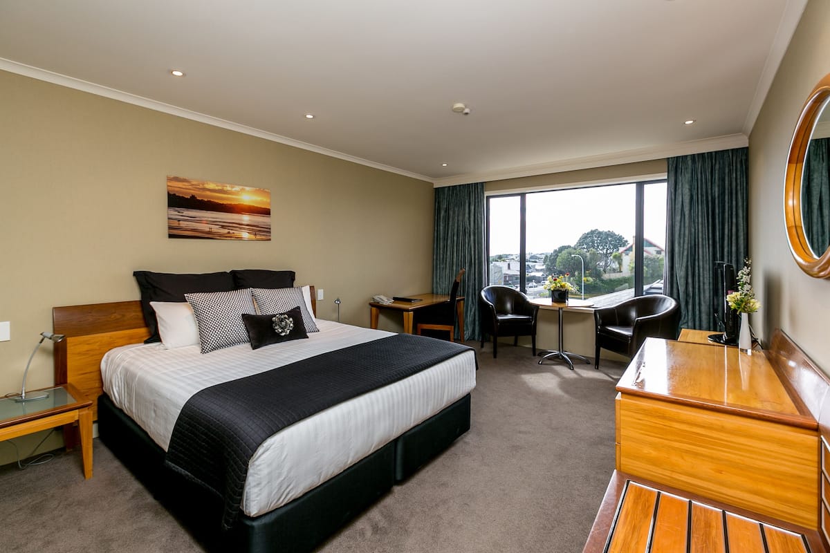 Ein Hotelzimmer mit einem großen Bett, einem Schreibtisch, einem Sessel und Blick auf die Stadt.