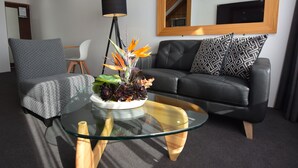 Una sala de estar moderna con una mesa de centro de vidrio, un sofá de cuero negro y una silla blanca.