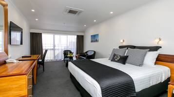 Une chambre d’hôtel avec un grand lit, un bureau avec un téléphone, une chaise, une petite table avec un vase et une fenêtre avec des rideaux.