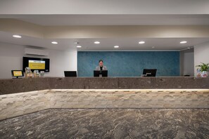 Zona de recepción con recepcionista, pantalla digital y pared de acento azul.