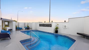 A swimming pool with a tiled edge, surrounded by lounge chairs and a bench.