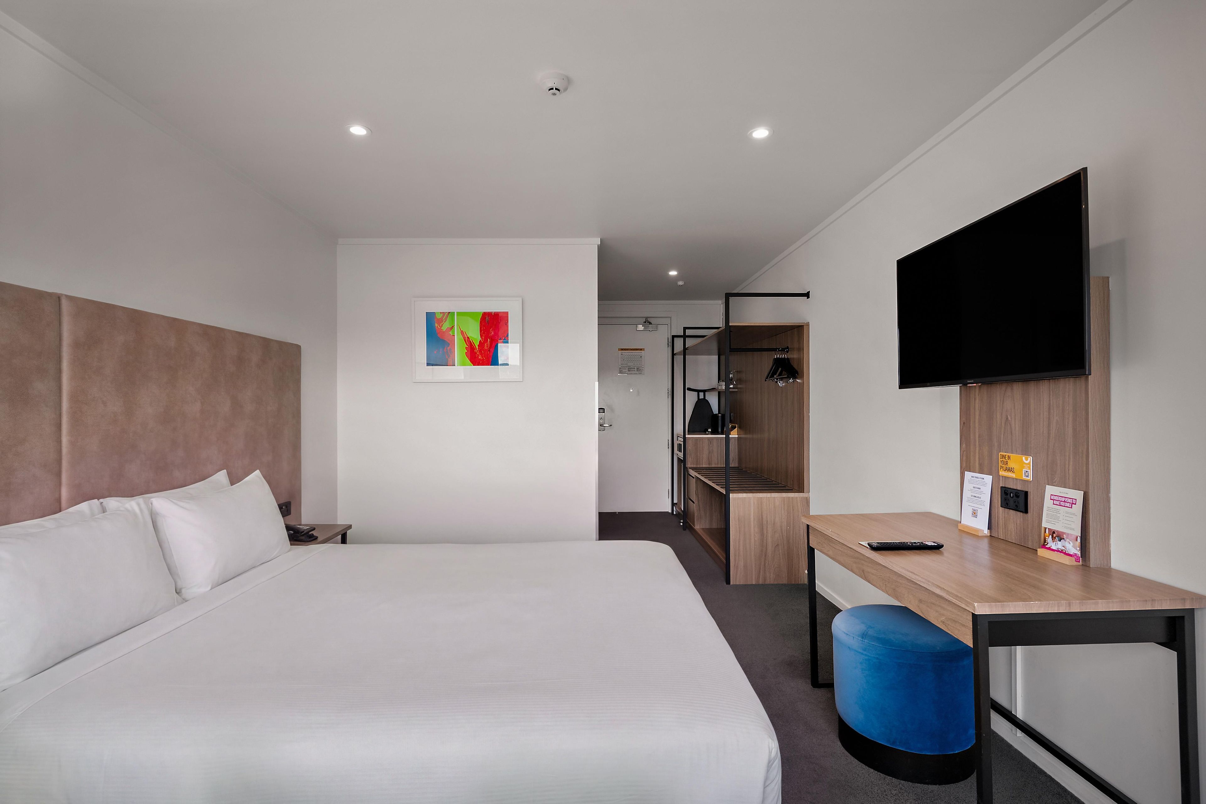Una camera d'albergo con un letto, una scrivania, una sedia, un televisore e un piccolo quadro appeso al muro.