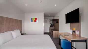 Una camera d'albergo con un letto, una scrivania, una sedia, un televisore e un piccolo quadro appeso al muro.