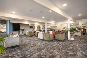 Un espacio interior amplio con varios arreglos de asientos, incluyendo sofás y sillones, y piso alfombrado.