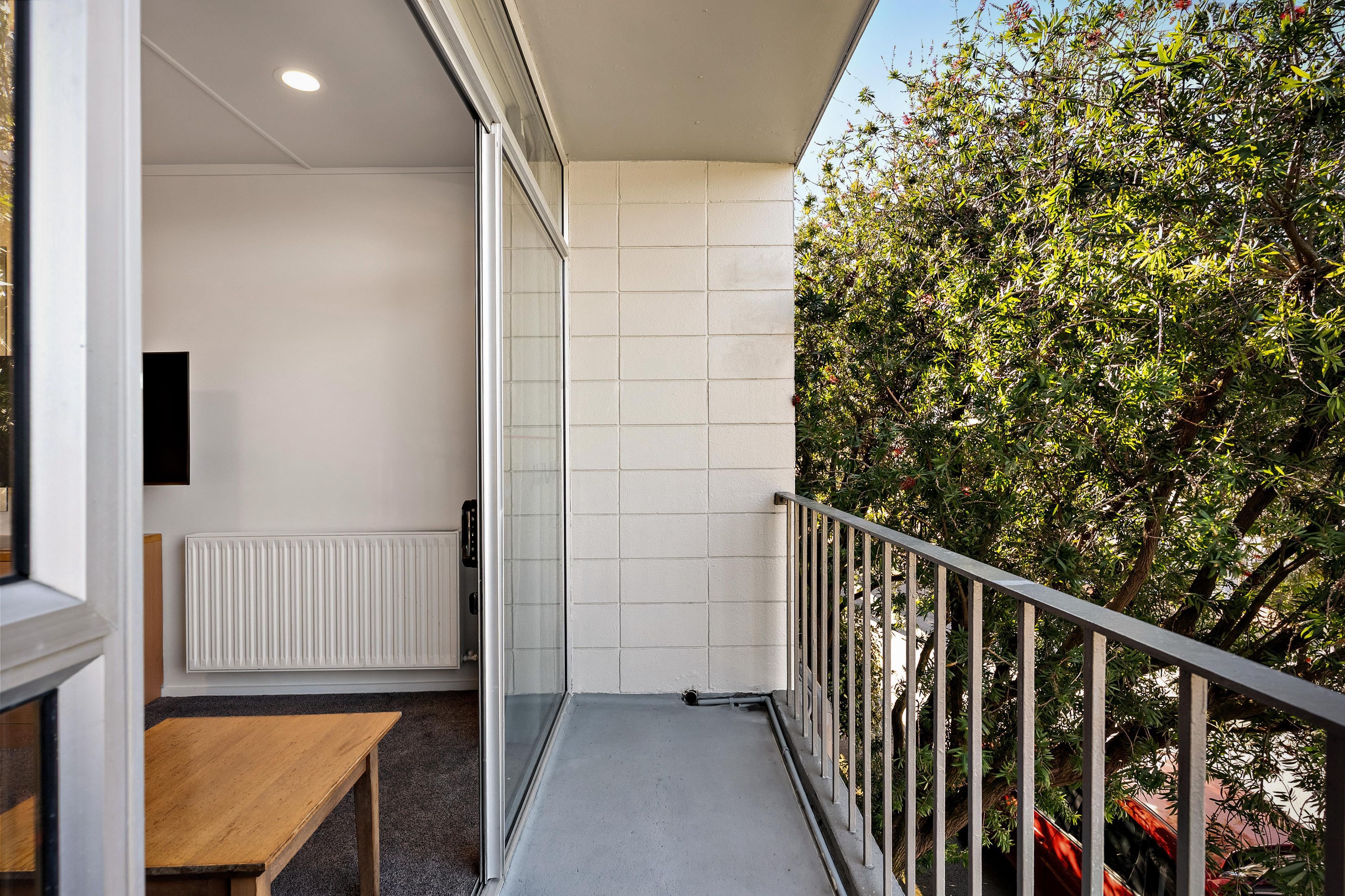 A balcony with a view of trees, a white wall, and a metal railing.