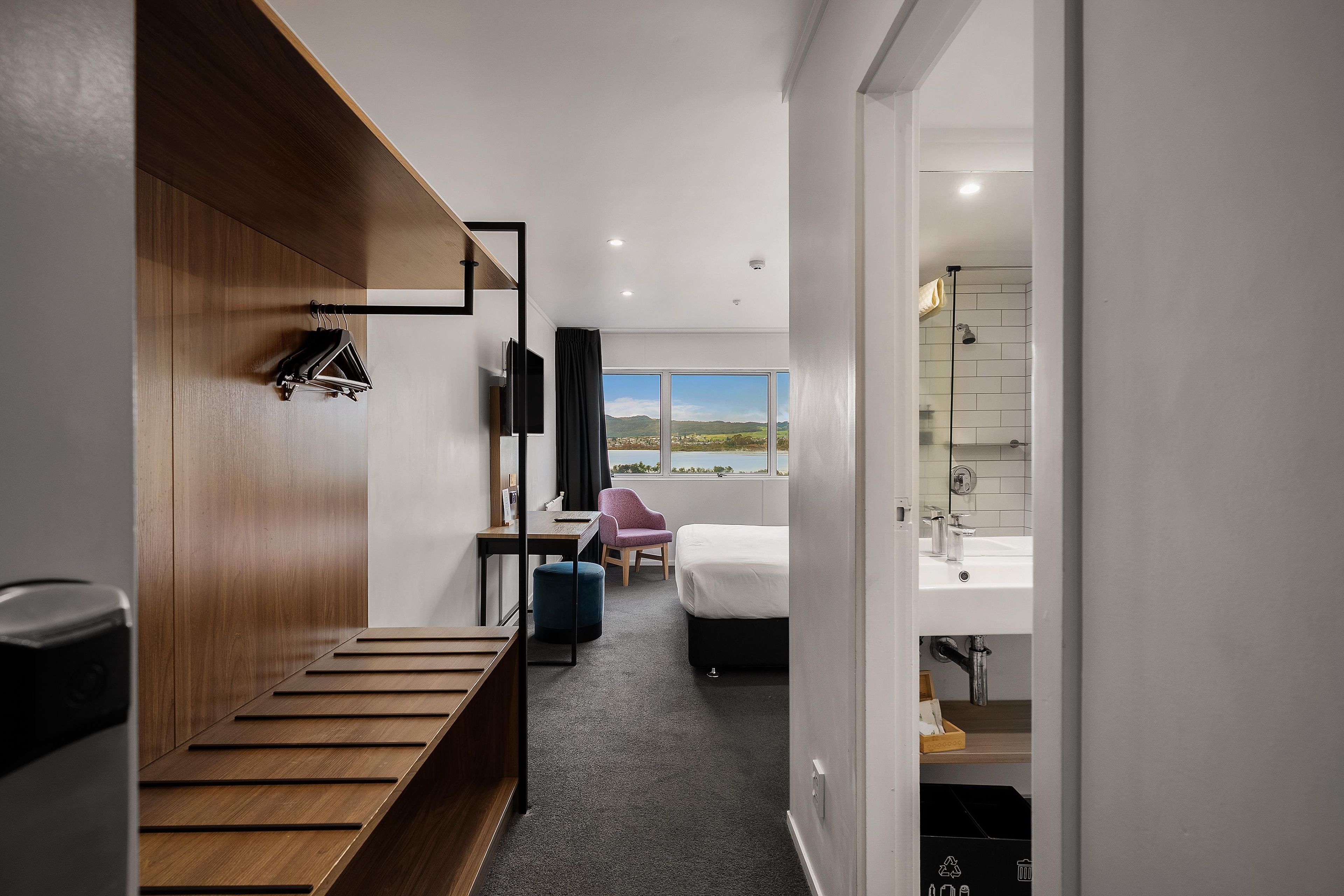 Une chambre d’hôtel avec un banc en bois, un lit, un bureau, une chaise et une vue sur l’extérieur.