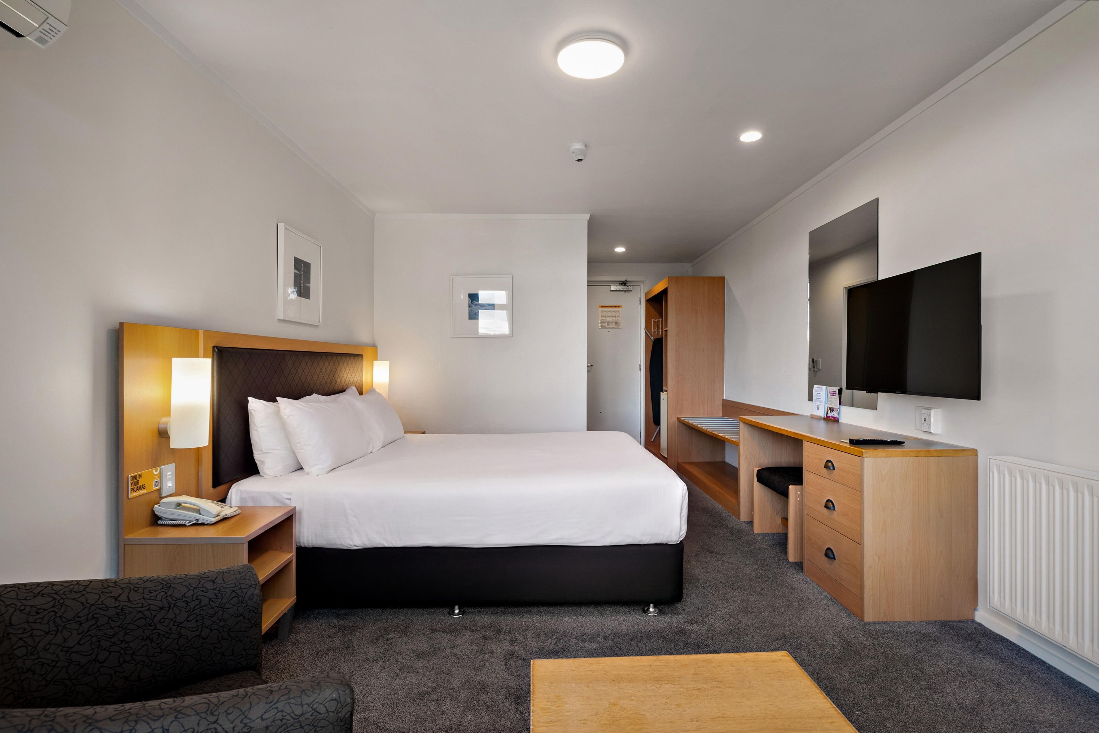 A hotel room with a bed, bedside table, lamp, desk, chair, and a television.