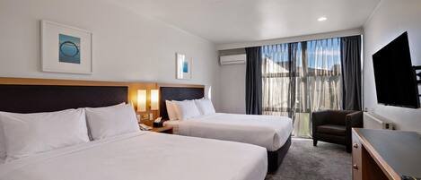 A hotel room with two beds, a desk, a chair, a TV, and a window with curtains.