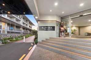 Entrada de un hotel con un cartel de 'Sudima Hotels', una estatua grande y una escalera que conduce a la recepción.