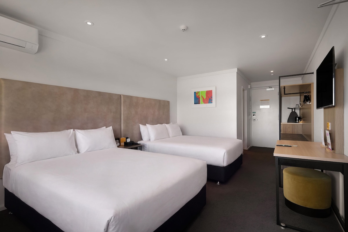 A hotel room with two beds, a desk, a chair, a TV, and a painting on the wall.