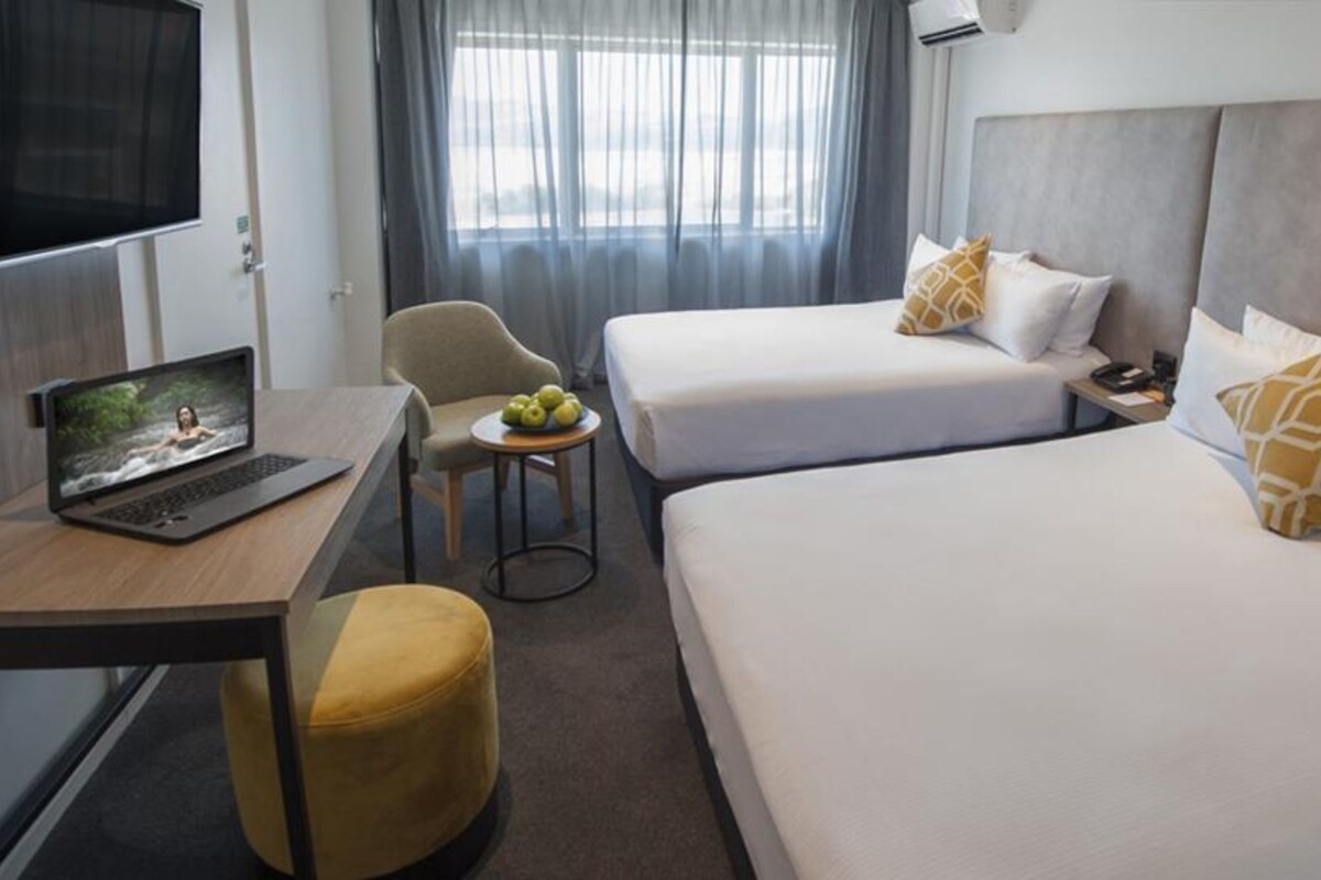 A hotel room with a desk, laptop, two beds, a chair, and a small table with apples.