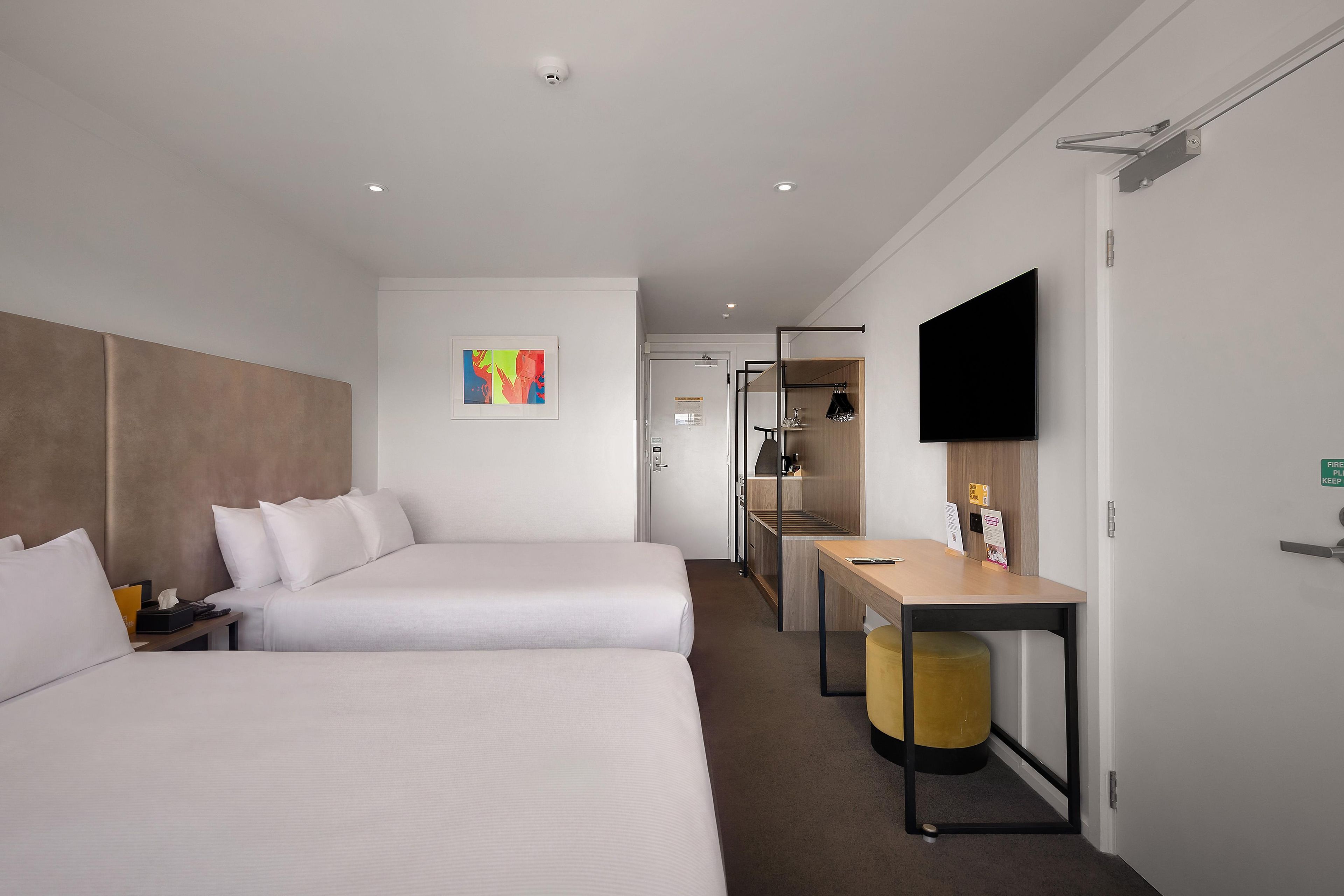 Habitación de hotel con dos camas, un escritorio, un televisor y un taburete pequeño.
