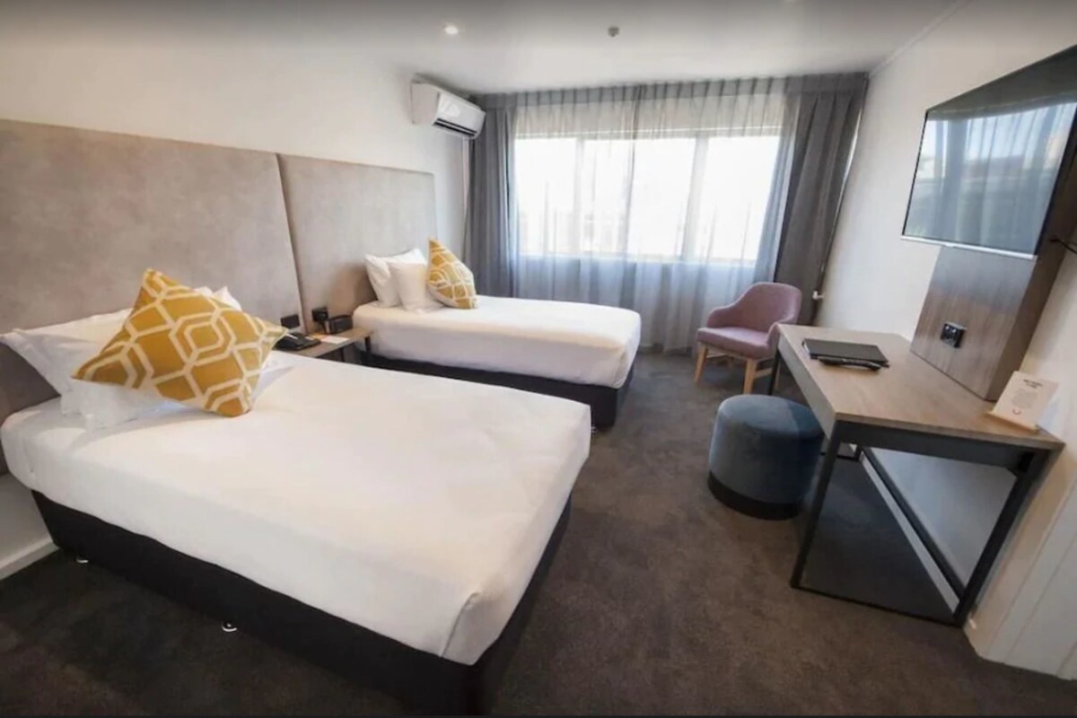 Una habitación de hotel con dos camas, un escritorio, una silla y un televisor.