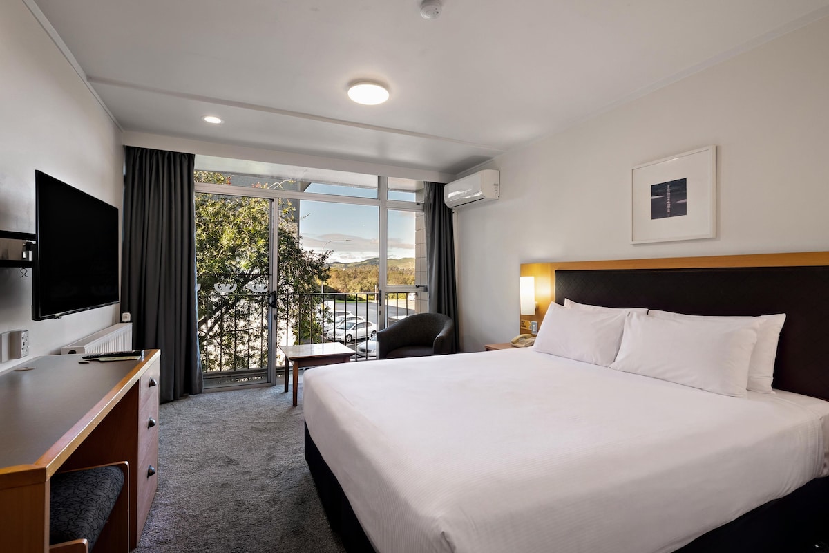 A hotel room with a large bed, a desk with a TV, a chair, and a view of the outdoors.
