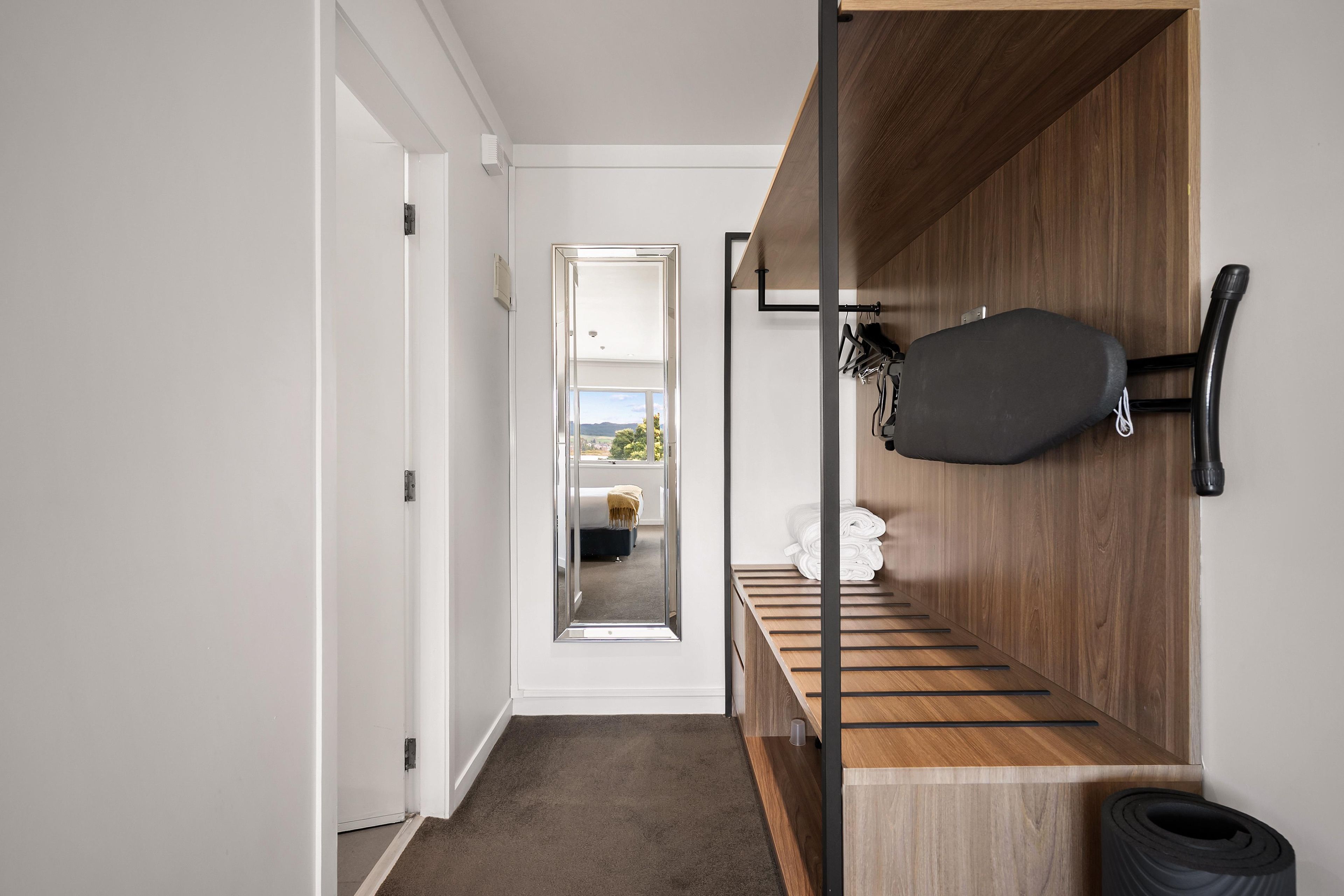 A hallway with a wooden bench, a wall-mounted coat rack, and a door leading to a room with a bed and a view of the outdoors.
