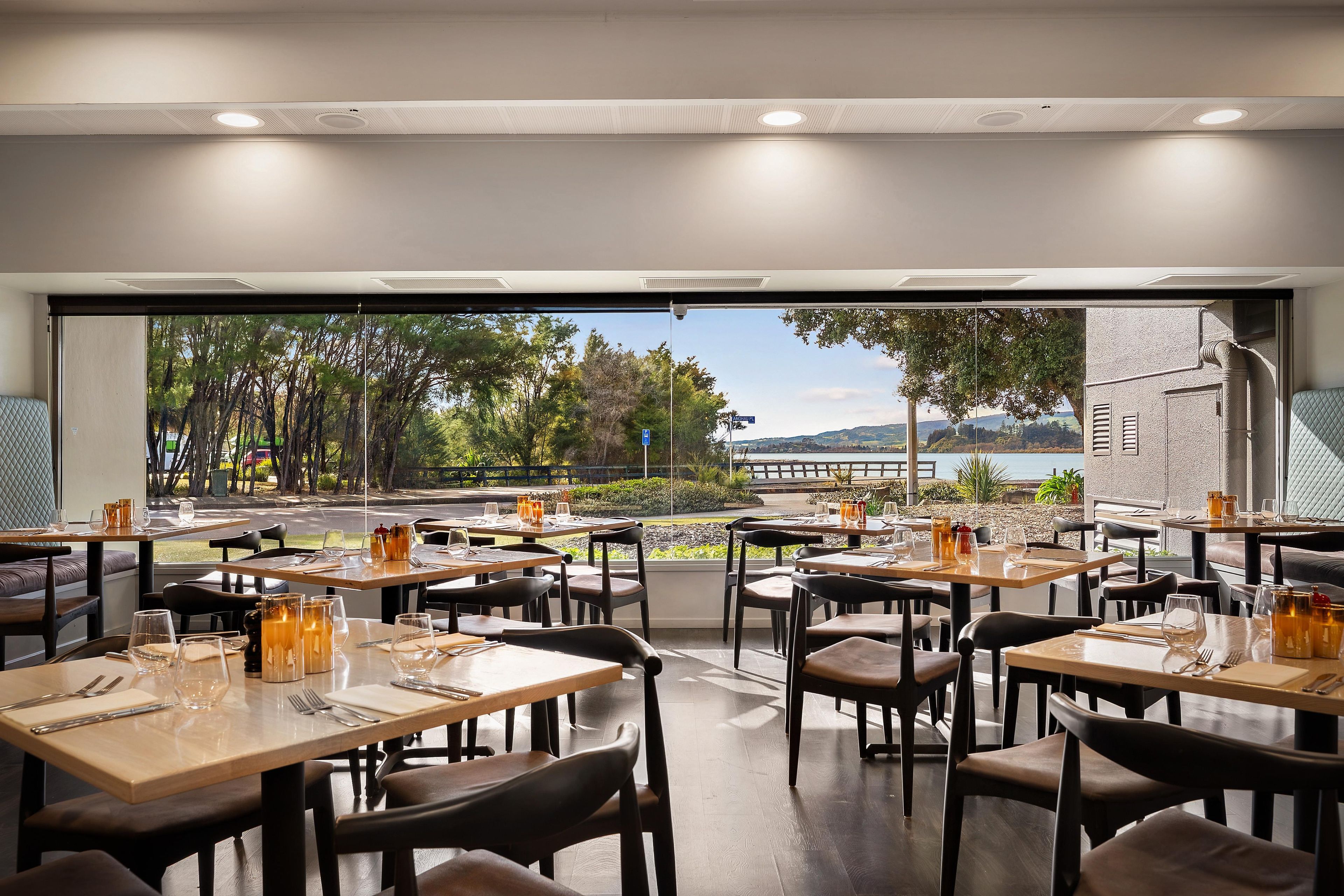 A restaurant with tables set for dining, a view of a lake, and a clear sky.