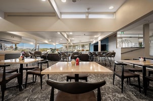 Uma ampla área de jantar com várias mesas e cadeiras, um espaço de bar e vista para o exterior.