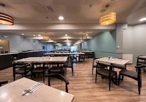 Un restaurante espacioso con numerosas mesas y sillas, una zona de mostrador e iluminación colgante.