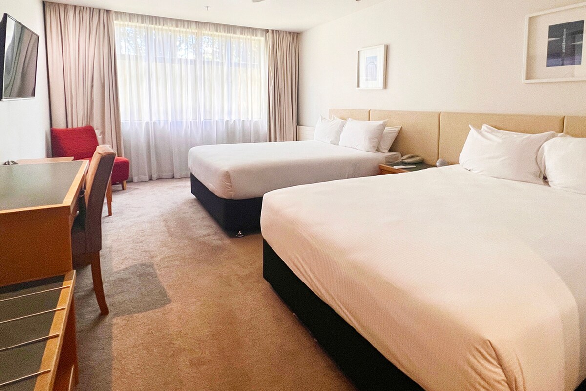 A hotel room with two beds, a desk, a chair, and a TV.