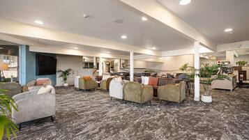 Un espacio interior amplio con varios arreglos de asientos, incluyendo sofás y sillones, y piso alfombrado.