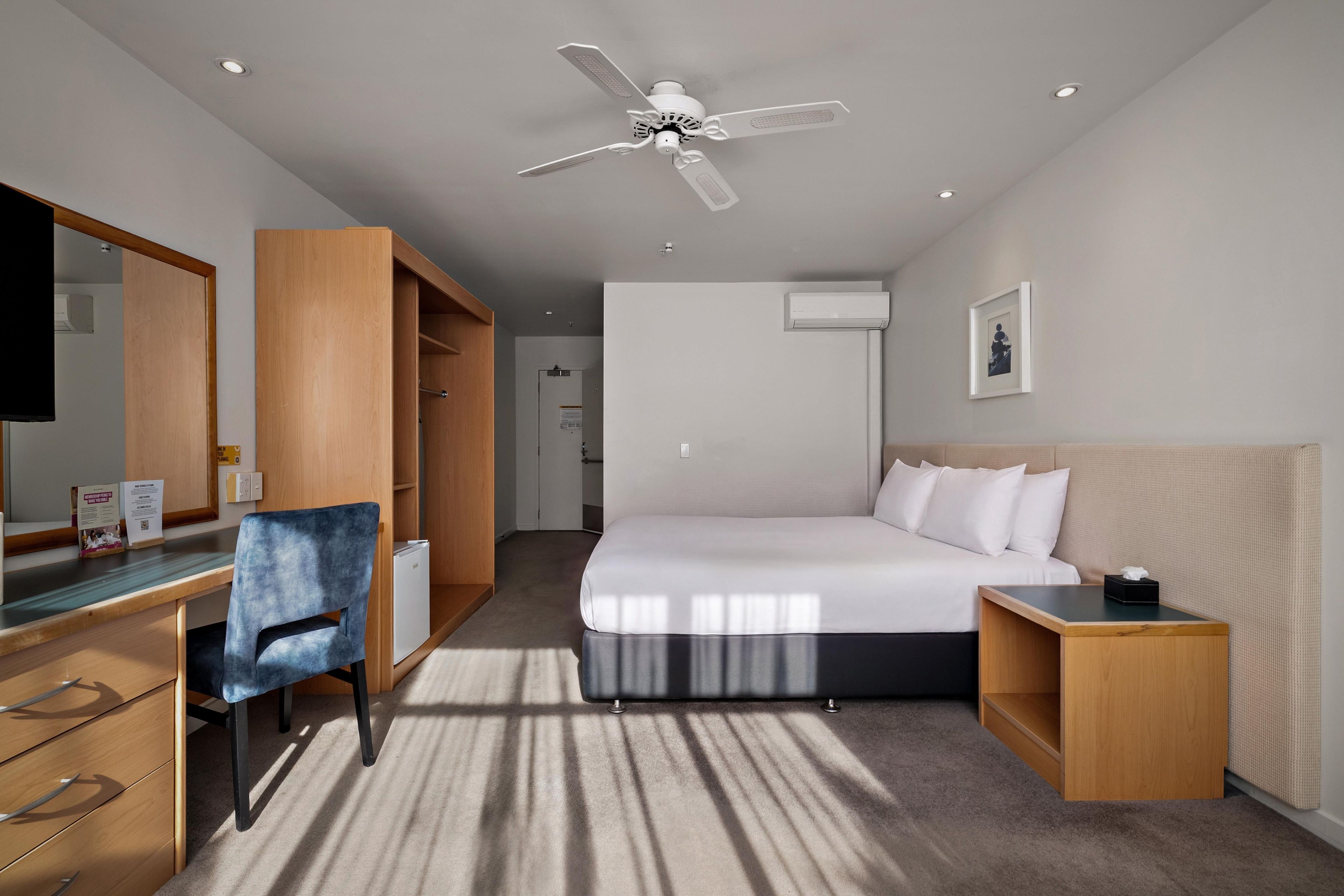 Une chambre d’hôtel équipée d’un lit, d’un bureau, d’une chaise, d’une armoire, d’un ventilateur de plafond et d’un appareil de climatisation.