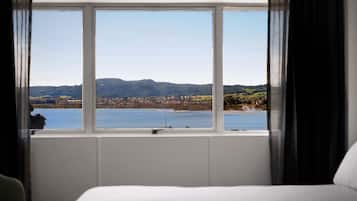 A hotel room with a large window offering a view of a lake and distant hills.