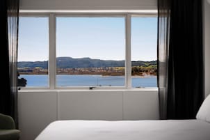 Een hotelkamer met een groot raam en uitzicht op een meer en heuvels in de verte.