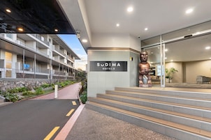 Entrada de un hotel con un cartel de 'Sudima Hotels', una estatua grande y una escalera que conduce a la recepción.