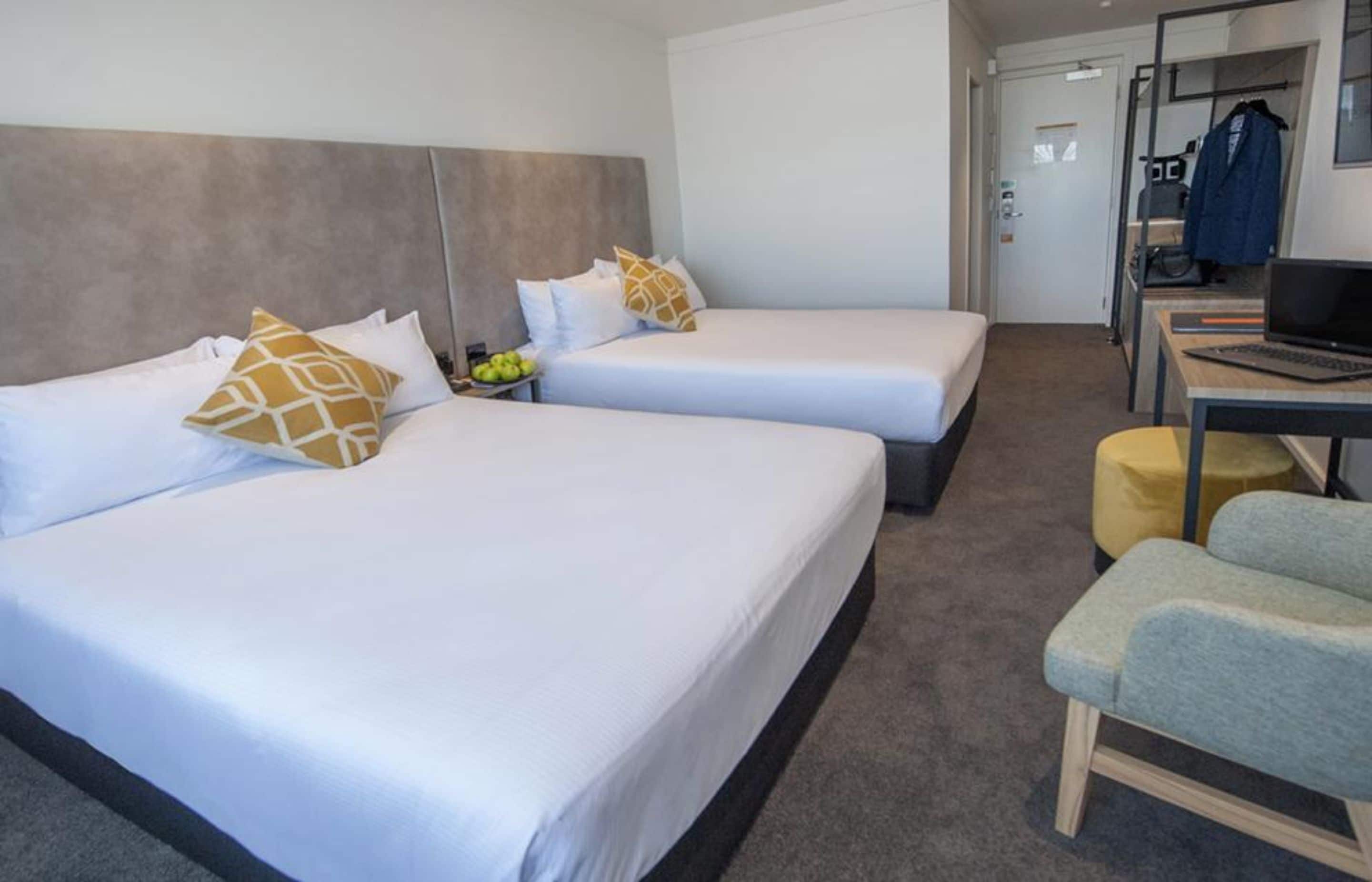 A hotel room with two beds, a desk, a chair, and a laptop.