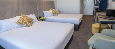 A hotel room with two beds, a desk, a chair, and a laptop.