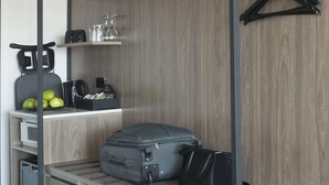 Habitación de hotel pequeña con una pared de madera, un perchero para equipaje, un escritorio con hervidor de agua, cafetera y algunas manzanas.
