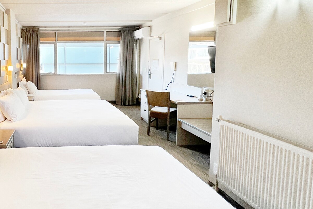 A hotel room with two beds, a desk, a chair, and a window with curtains.