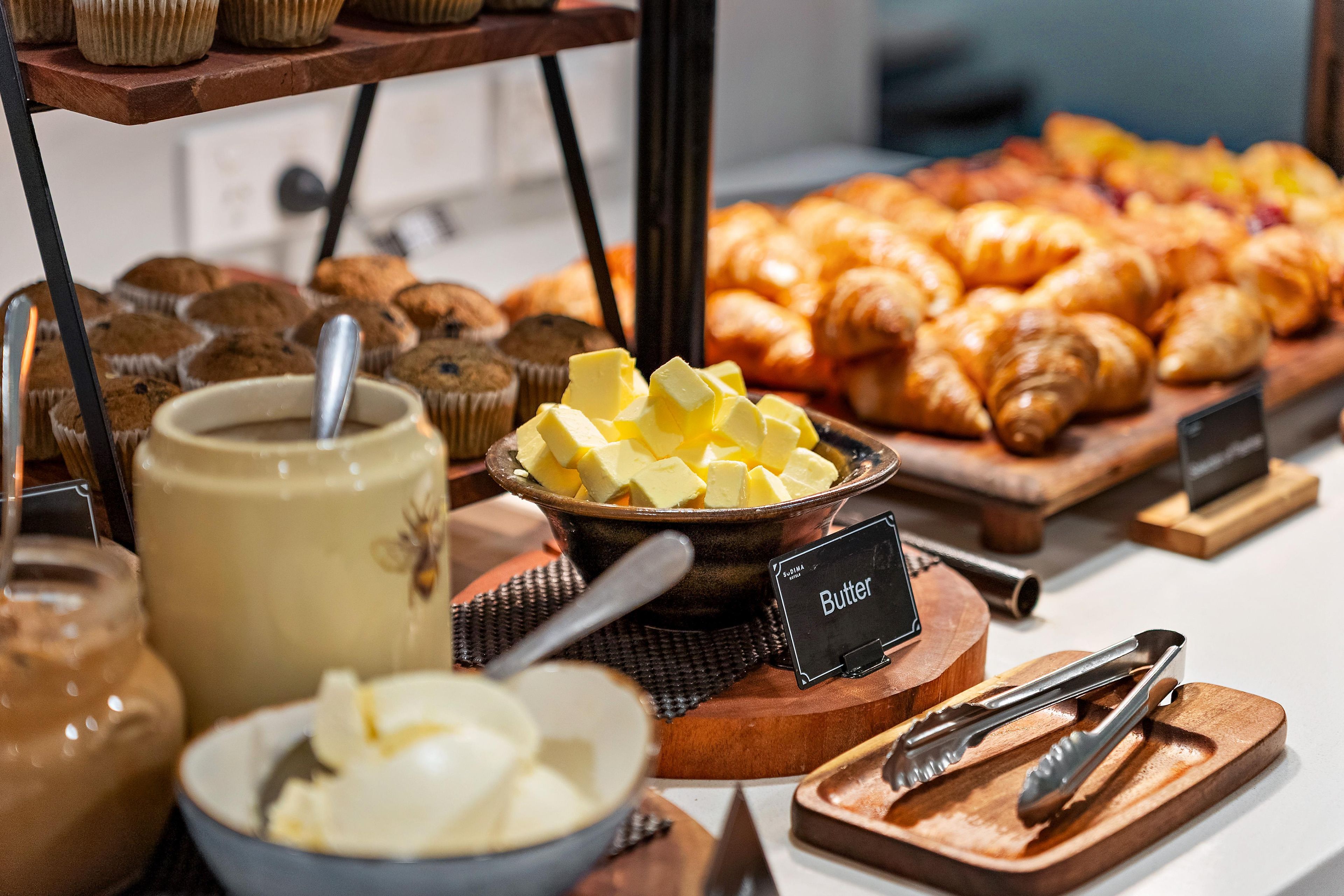 A buffet with various baked goods including muffins, croissants, and butter.