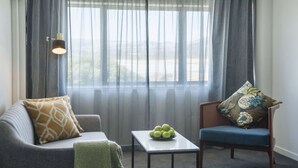 Una habitación con sofá, una silla, una mesita con un cuenco de manzanas y una lámpara.