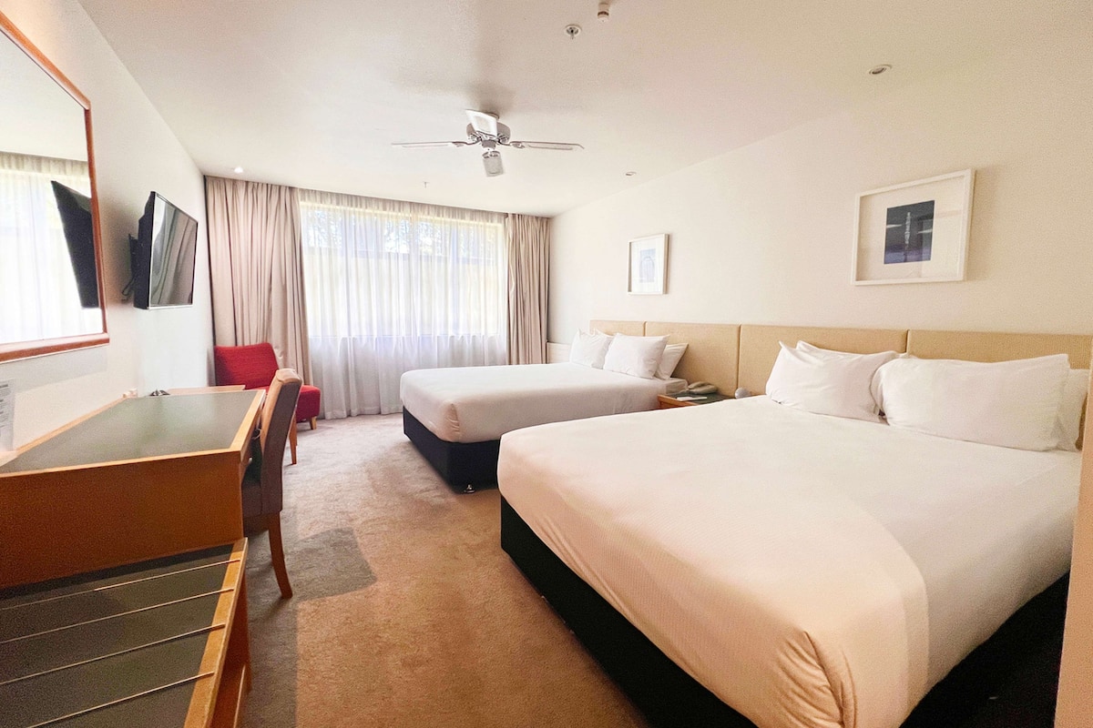 A hotel room with a bed, a desk, a chair, a ceiling fan, and a window with curtains.
